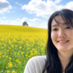 Photo image Kayoko Shoji in front of field of flowers and bright blue sky